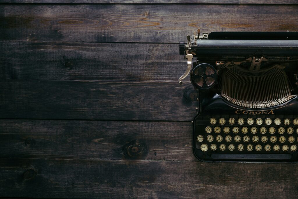 Photo of a typewriter sitting on a dark wood brown desk.