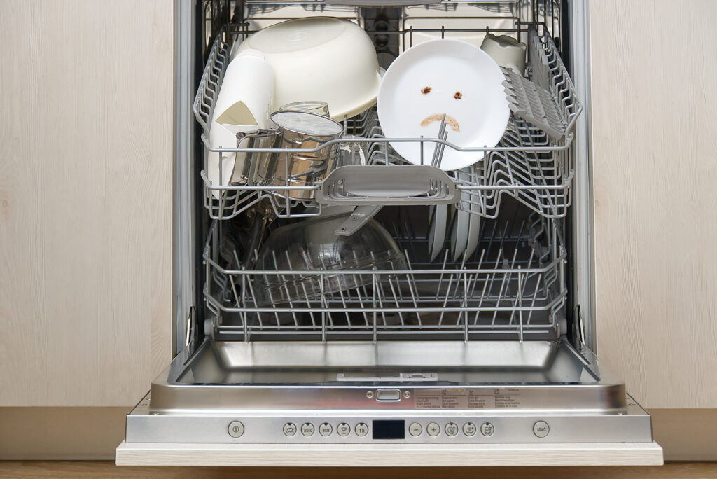 open dishwasher with a dirty plate that has a sad face 