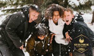 A family of four smiling and laughing huddled together in the snow with H2O Solutions logo