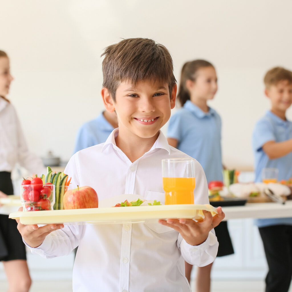Kid holding school lunch in cafeteria and smiling