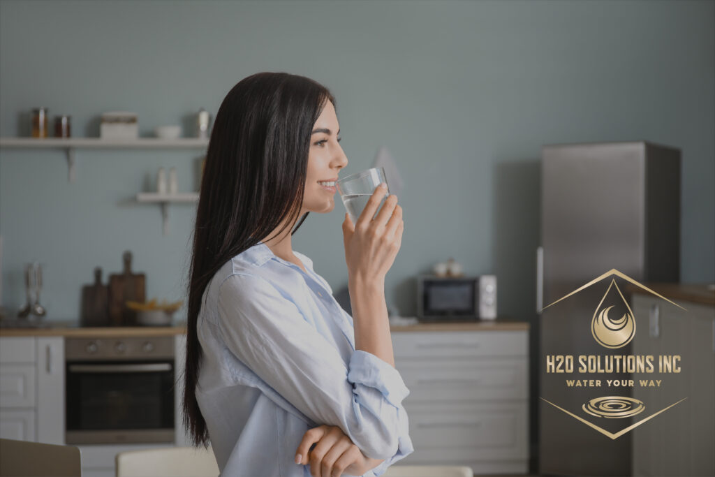 Woman drinking water in kitchen with H2O solutions logo overlayed